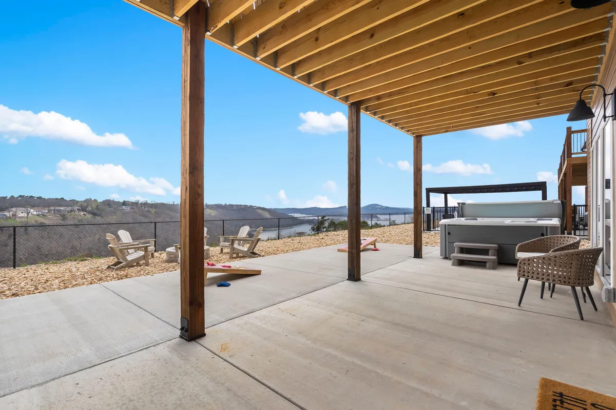 This image showcases a spacious wooden deck complete with a bubbling hot tub, lounge chairs, and a stunning landscape view that includes glimpses of the lake and natural surroundings.