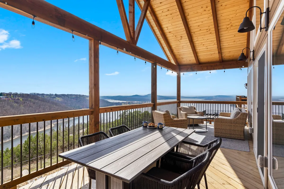 The image features an outdoor dining table under wooden ceiling beams, with comfortable seating arranged to enjoy a scenic view. The atmosphere is tranquil, ideal for al fresco dining or gathering at sunrise and sunset. The setting connects the indoors to the natural beauty outside, emphasizing the social and culinary experience.