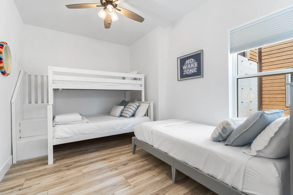 A playful and comfortable bunk room with a bunk bed, single bed, and a window letting in natural light. The room is decorated with cheerful artwork and includes a ceiling fan for comfort, capturing a sense of fun and togetherness for younger guests.