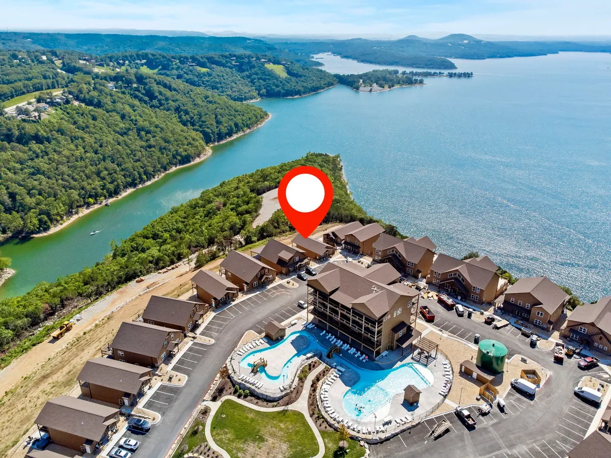 An exterior scene featuring a swimming pool overlooking the lake, with surrounding hills and a building structure in the background. The setting invites guests to enjoy both poolside relaxation and lakeside adventures.