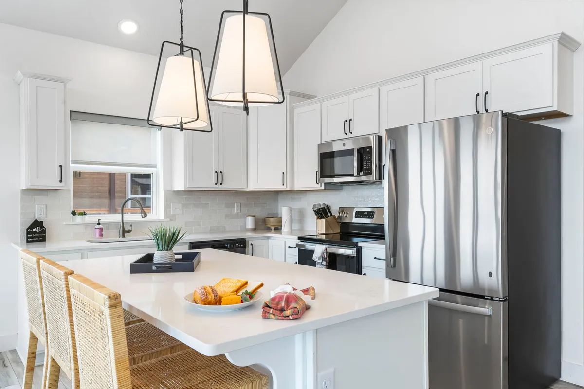 This inviting kitchen features a spacious island countertop, stainless steel appliances, pendant lighting, and a tempting bowl of pastries and fruit. The layout is open and welcoming, suggesting opportunities for cooking together, entertaining, and enjoying fresh local ingredients.