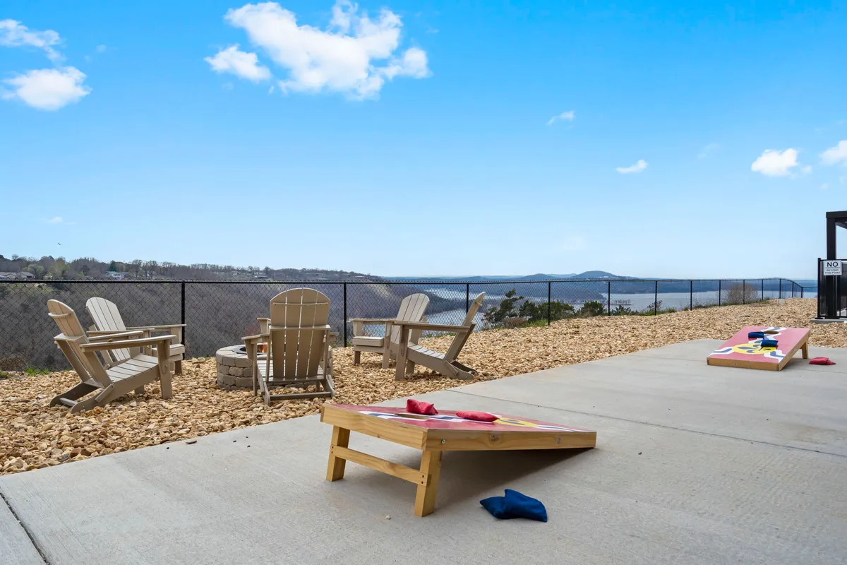 A cozy outdoor firepit area surrounded by Adirondack chairs, with a cornhole game set up and scenic views of rolling hills in the background. The space encourages socializing, storytelling, and relaxed evenings under the stars.
