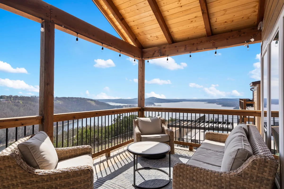 The hero image showcases the exterior of a brand-new single-family house nestled on Wilderness Mountain, with a spacious outdoor seating area under a warm wooden ceiling. The seating area opens up to breathtaking, unobstructed lake views, inviting guests to relax, entertain, or soak in the serenity of the landscape. The tranquil setting is perfect for stargazing at night, watching sunrises with coffee, or hosting lively summer barbecues—all set against the peaceful backdrop of Kimberling City’s natural beauty.