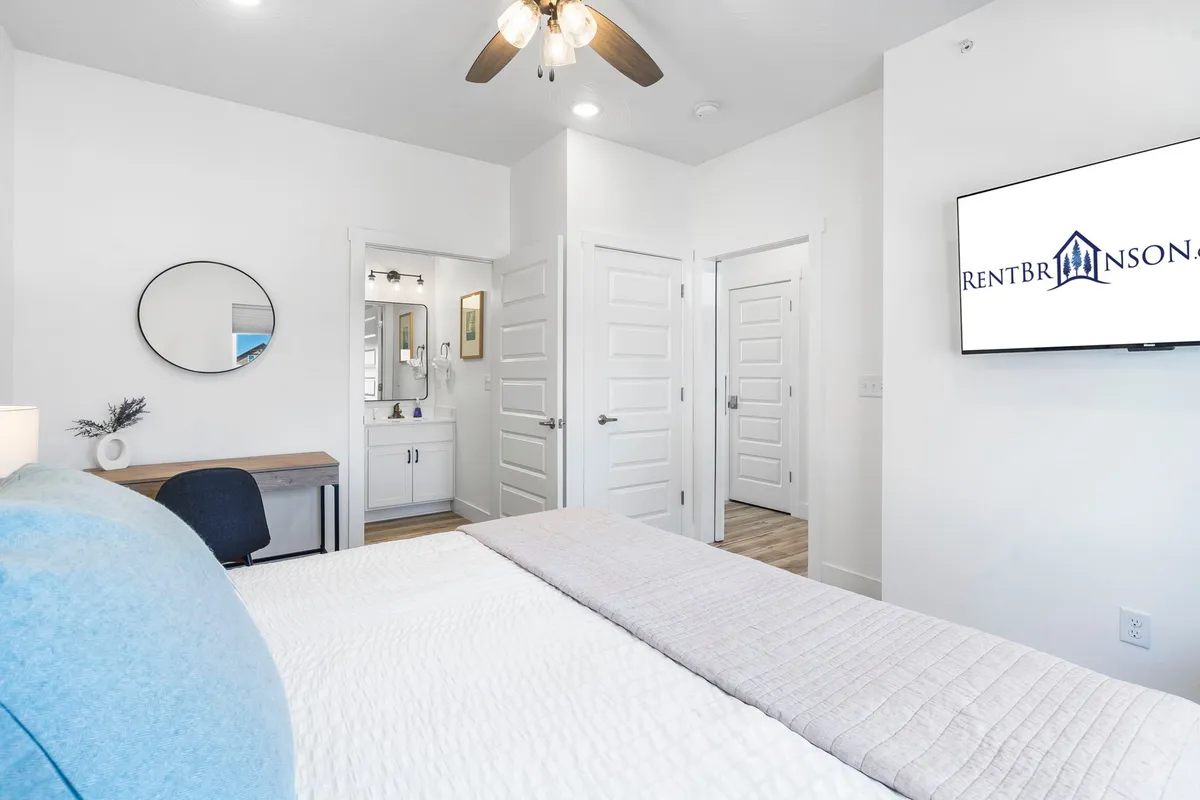 A calm, cozy bedroom featuring a plush bed, TV, mirror, and vanity. Soft lighting and restful decor create an inviting space perfect for unwinding after a busy day. The space exudes tranquility and privacy, ideal for adult guests.