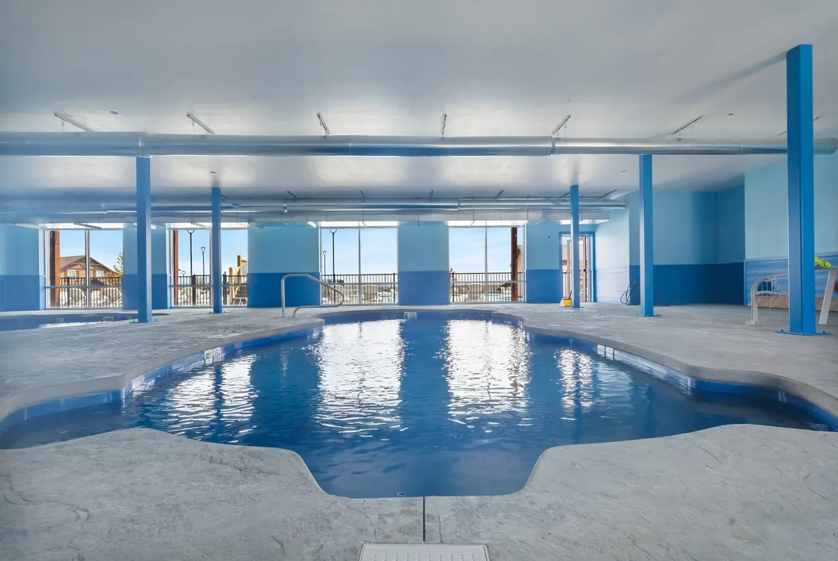 An interior view of the all-season indoor pool, with large windows that let in natural light and blue walls that create a refreshing atmosphere. Guests are seen swimming and relaxing by the poolside, illustrating year-round aquatic enjoyment.