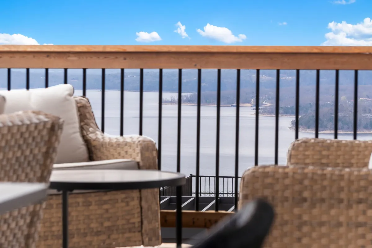 An inviting deck with outdoor seating overlooks a serene lake, framed by a wooden railing. The space is perfect for peaceful mornings, meditation, or simply soaking up the tranquil lake view.